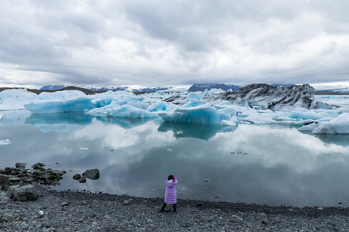 A person photographing Jokulsarlon, a glacial lagoon with icebergs in southern Iceland. Jokulsarlon formed around 1935 and the size of the lake keeps increasing due to the melting glaciers.