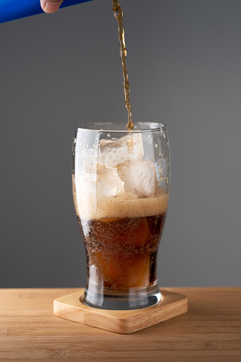 Canned pouring a soft drink into a drinking glass with ice cubes