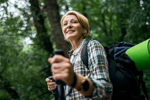 mid adult woman in the forest hiking with hiking poles - mid aged woman imagens e fotografias de stock