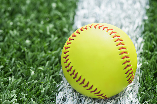 A new yellow softball sitting on the white baseline during a day game