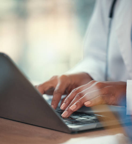 doctor working on their laptop in the hospital. hands of a doctor typing on their computer sitting at the desk. closeup on hands of medical professional working online on a wireless laptop - medical record imagens e fotografias de stock