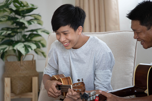 Activities , An Asian family consists of father, daughter and son enjoying music, singing, dancing, playing guitar.