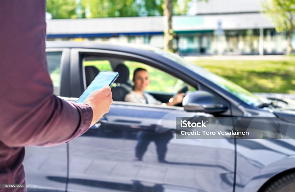 Taxi phone app for cab or car ride share service. Customer waiting driver to pick up on city street. Man holding smartphone. Taxi phone app for cab or car ride share service. Customer waiting driver to pick up on city street. Man holding smartphone. Mobile and online booking for rideshare transportation with cellphone. Car Stock Photo