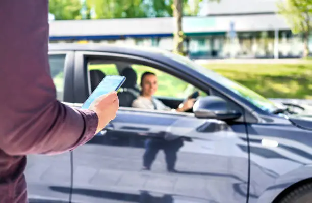 Taxi phone app for cab or car ride share service. Customer waiting driver to pick up on city street. Man holding smartphone. Mobile and online booking for rideshare transportation with cellphone.