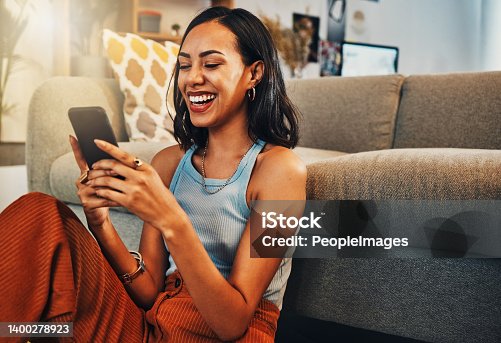 istock Beautiful mixed race woman browsing internet on cellphone in home living room. Happy hispanic sitting alone on floor in lounge and using technology to network. Laughing while scrolling on social media 1400278923