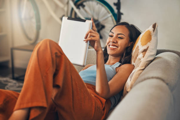 istock Smiling mixed race woman browsing internet on digital tablet at home. Happy hispanic lying down on living room sofa alone and using technology. Relaxed woman scrolling and searching online on weekend 1400278924
