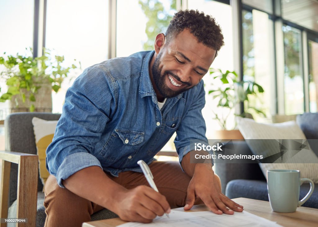 Happy bachelor signing a contract. Man filling out insurance documents. Handsome young man filling out banking papers. Hispanic young man filling out paperwork to invest insurance Form - Document Stock Photo