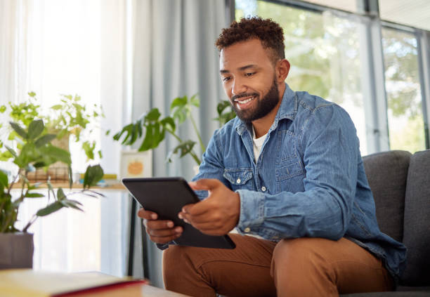istock Handsome bachelor reading on his digital tablet. Happy bachelor enjoying his day at home relaxing. Always connected to the online world with his wireless tablet. Young man resting on his couch 1400280367