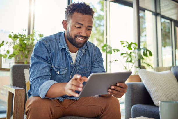 istock Hispanic man using his digital tablet at home. Young bachelor using his wireless device in his apartment. Handsome man browsing the internet on his digital tablet at home. Bachelor at home alone 1400280378