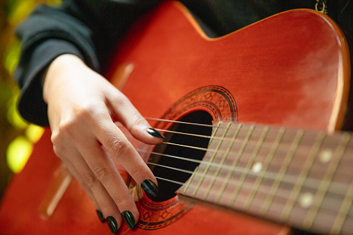 Young woman playing acoustic guitar close up finger