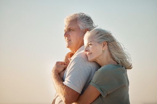 couple embracing on the beach. Mature couple enjoying the view on the beach. Senior couple bonding on the beach. Mature couple being affectionate on the beach. Senior couple on vacation by the sea