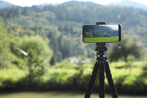 Taking photo of beautiful mountain landscape with smartphone mounted on tripod outdoors