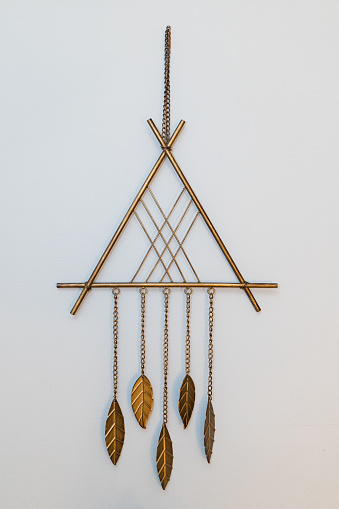 A triangle shaped wall hanging with geometric designs and dangling chime leaves.