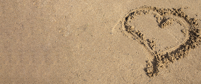 A heart drawn in the sand. Beach background. Top view, space for text.
