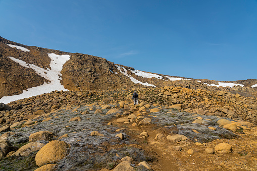 Man hiking up the ridge of Hveradalir  geothermal area against blue sky on sunny day, Iceland