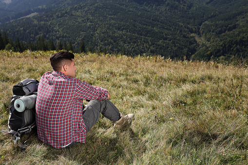 Tourist with backpack sitting on ground and enjoying landscape in mountains, back view