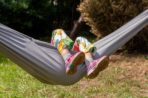 Anonymous child, school age girl laying on a hammock feet legs up, face obscured, outdoors scene, summer fun and leisure, resting, boredom abstract concept, shoes closeup, vacation, holidays