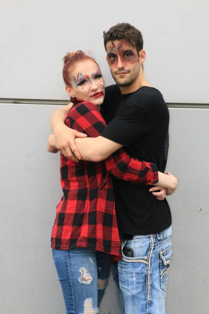 A Caucasian couple ready for Halloween in an embrace. She is wearing a red plaid shirt and he is wearing a black tshirt.