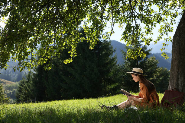 istock Young woman reading book under tree on meadow in mountains 1400289578