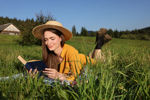 Beautiful young woman reading book on green meadow