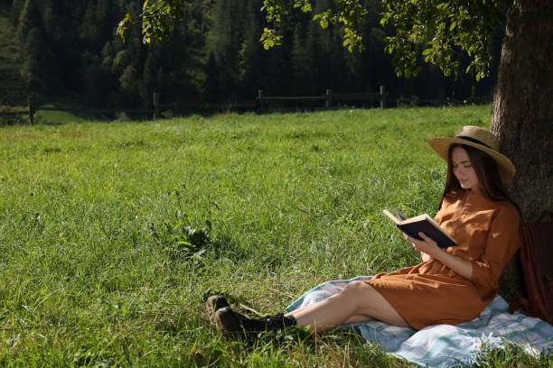 istock Young woman reading book under tree on meadow near forest 1400290270
