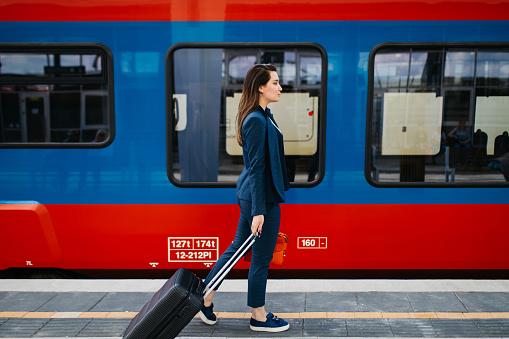 A young beautiful businesswoman with suitcase in her hand is waiting for her train to arrive.