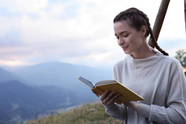 istock Beautiful young woman reading book in mountains, space for text 1400290418