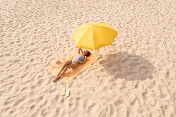istock Woman resting under yellow beach umbrella at sandy coast 1400290747