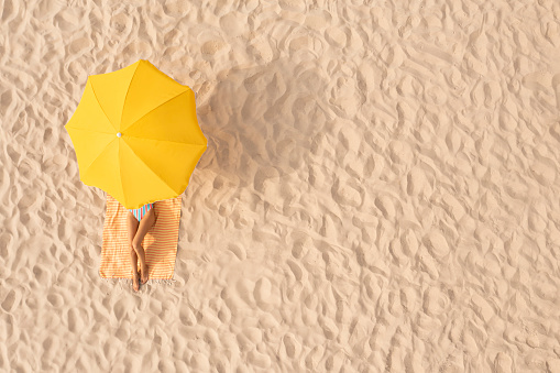 Woman resting under yellow beach umbrella at sandy coast, aerial view. Space for text