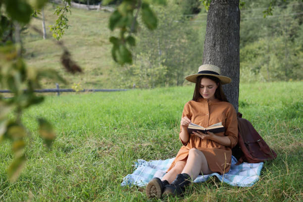 istock Young woman reading book under tree on meadow 1400291089