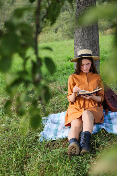 istock Young woman reading book under tree on meadow 1400292492