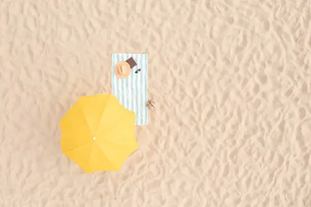 Photo of Beach umbrella near towel and other vacationist's stuff on sand, aerial view. Space for text