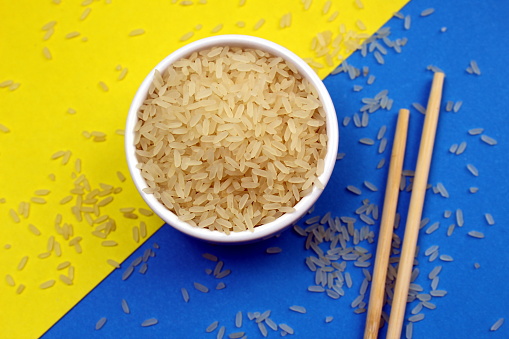 Dry rice lies in a white bowl with wooden sticks.