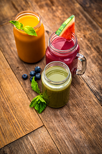 Three colorful fruit smoothie drinks in retro glass jar bottles on a old wooden background