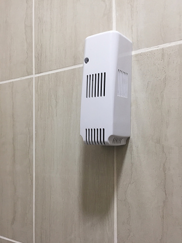 Automatic air freshener hanging on the ceramics tile bathroom wall