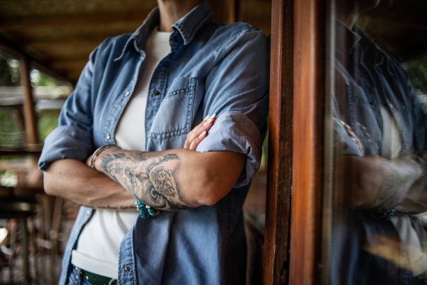 A portrait of an urban mature woman with crossed arms, who has a tattoo on her left arm, dressed in her casual style.
