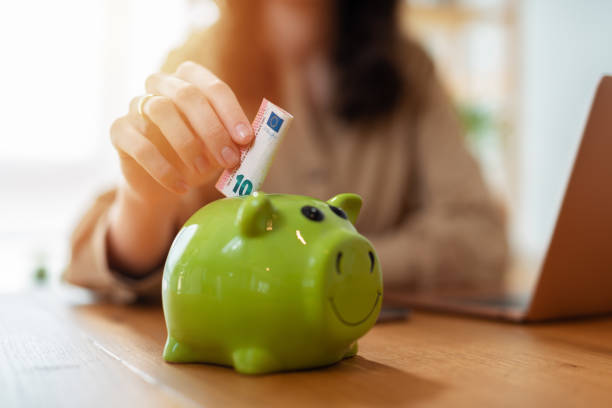 Close up young female putting coin in piggy bank. Woman saving money for household payments, utility bills, calculating monthly family budgets, making investments or strategy for personal savings stock photo