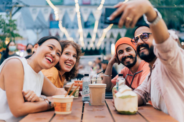Friends Taking A Selfie Group of friends taking a selfie outdoors using a smartphone. They are enjoying their time together. night market stock pictures, royalty-free photos & images