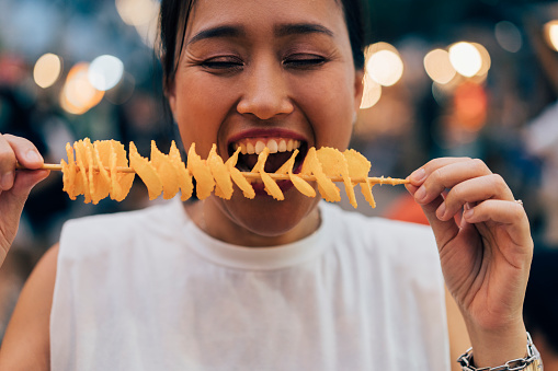 Close up shot of an Asian woman enjoying eating her chips.