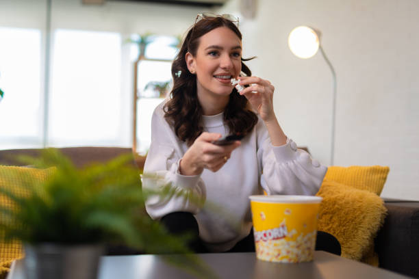 Young beautiful woman watching TV at home and eating pop corn stock photo
