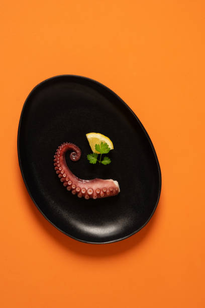 istock Grilled octopus plated with lemon and parsley on an orange background 1400302629