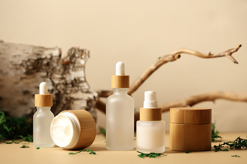 SPA natural organic cosmetics packaging design. Set of transparent glass bottles, moisturizer cream in wooden jars. Tree branch, birch bark and moss on background.