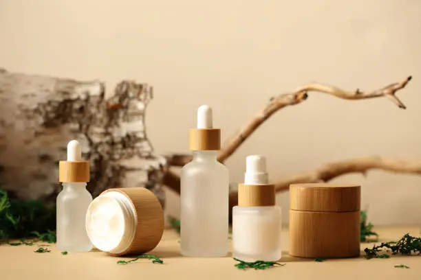 Photo of SPA natural organic cosmetics packaging design. Set of transparent glass bottles, moisturizer cream in wooden jars. Tree branch, birch bark and moss on background.