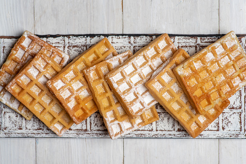 Belgian waffles sprinkled with sugar on a white board isolated on white. Top view. Stock photo.