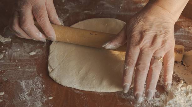 istock Women's hands with a rolling pin roll out the dough. Making homemade bread. 1400309551
