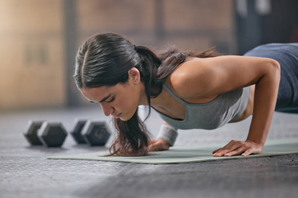 une jeune femme hispanique en forme faisant des exercices de push up au poids du corps tout en faisant de l’exercice dans un gymnase. athlète féminine concentrée faisant des pressions pour développer les muscles, améliorer le haut du corps, renforce - athlete push ups muscular build female photos et images de collection