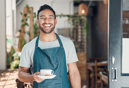 Retrato de un joven camarero hispano sirviendo una taza de café mientras trabajaba en un café. Barista amigable y propietario de un coffeeshop que administra una exitosa startup de restaurantes photo