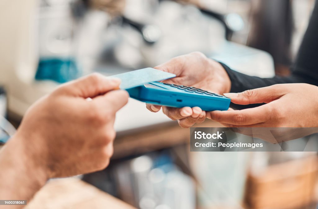 Closeup of a clerk accepting a contactless credit card payment using nfc technology from a customer in a cafe or store. Hands of man tapping card machine reader to process cashless transaction for a purchase in a shop Credit Card Stock Photo