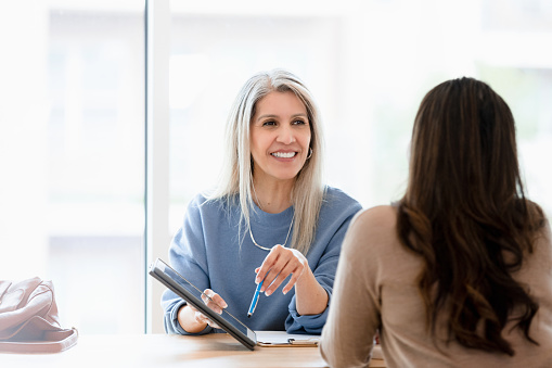 The cheerful mature adult female lawyer listens to the unrecognizable female client.