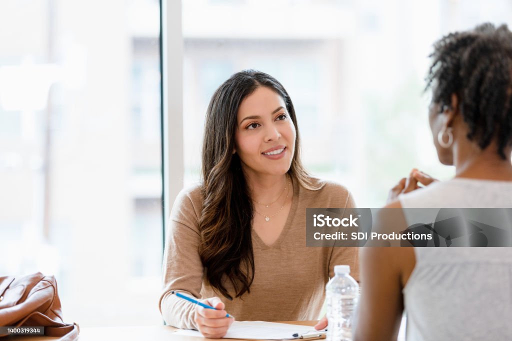 Mid adult female manager interviews unrecognizable woman for job A mid adult female manager smiles and listens attentively to an unrecognizable woman during the interview. Interview - Event Stock Photo